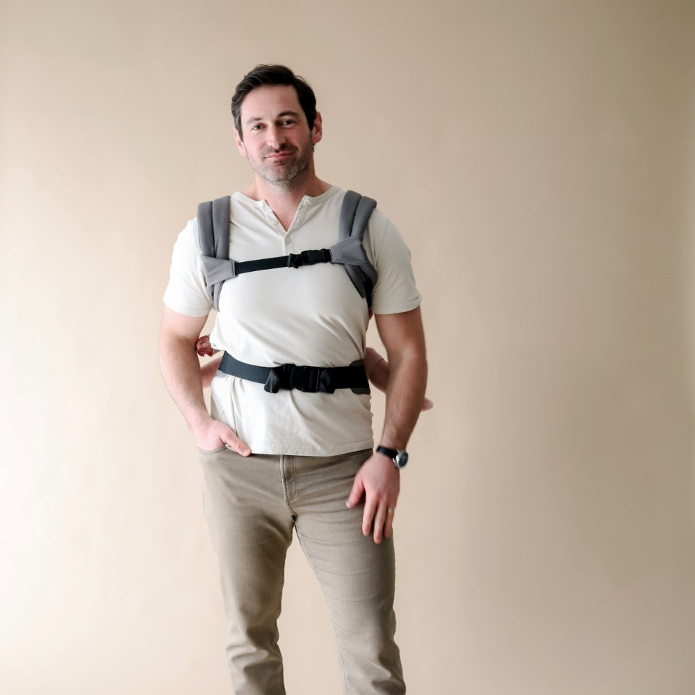 Man wearing a baby carrier against a plain background