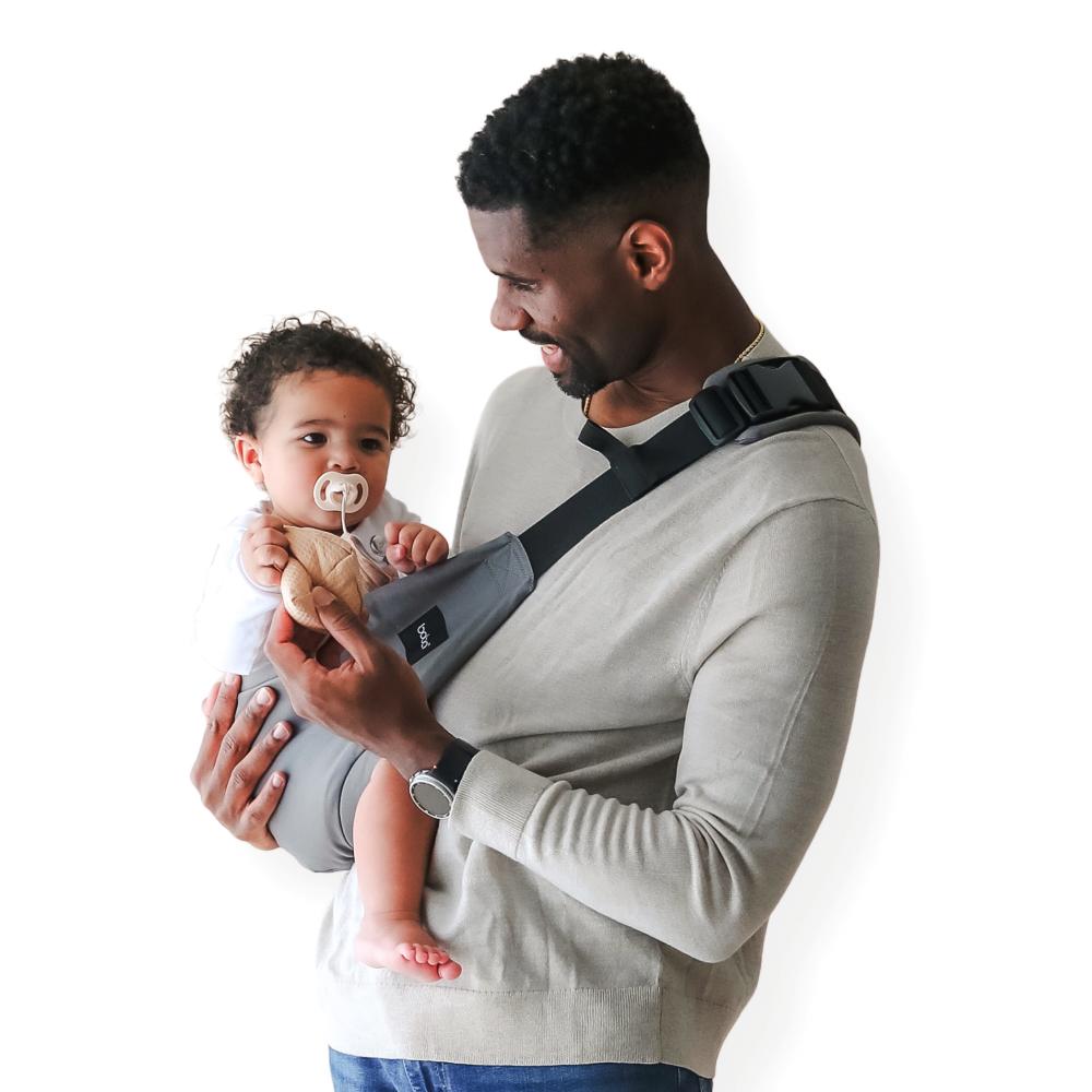 Man holding a baby in a Boba Buddy carrier assist hip carrier against a white background