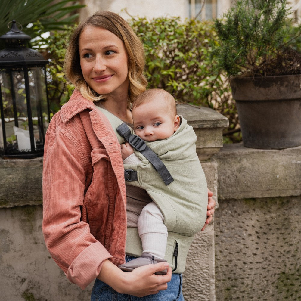 Woman holding a baby in a green linen carrier outdoors