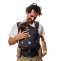 Man carrying a child in a Boba X baby carrier in Cosmos print with a white background