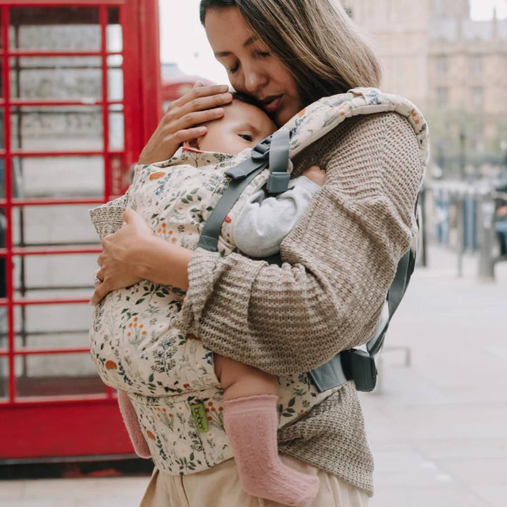 Woman carrying a child in a baby carrier with a red telephone box in the background