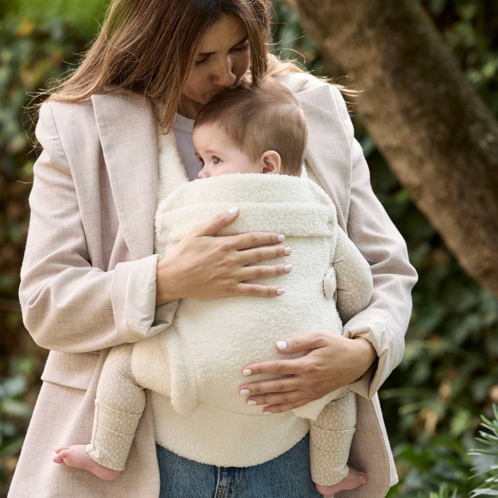 Woman holding a baby in a high fashion baby carrier made from cream coloured boucle fabric in an aesthetic style