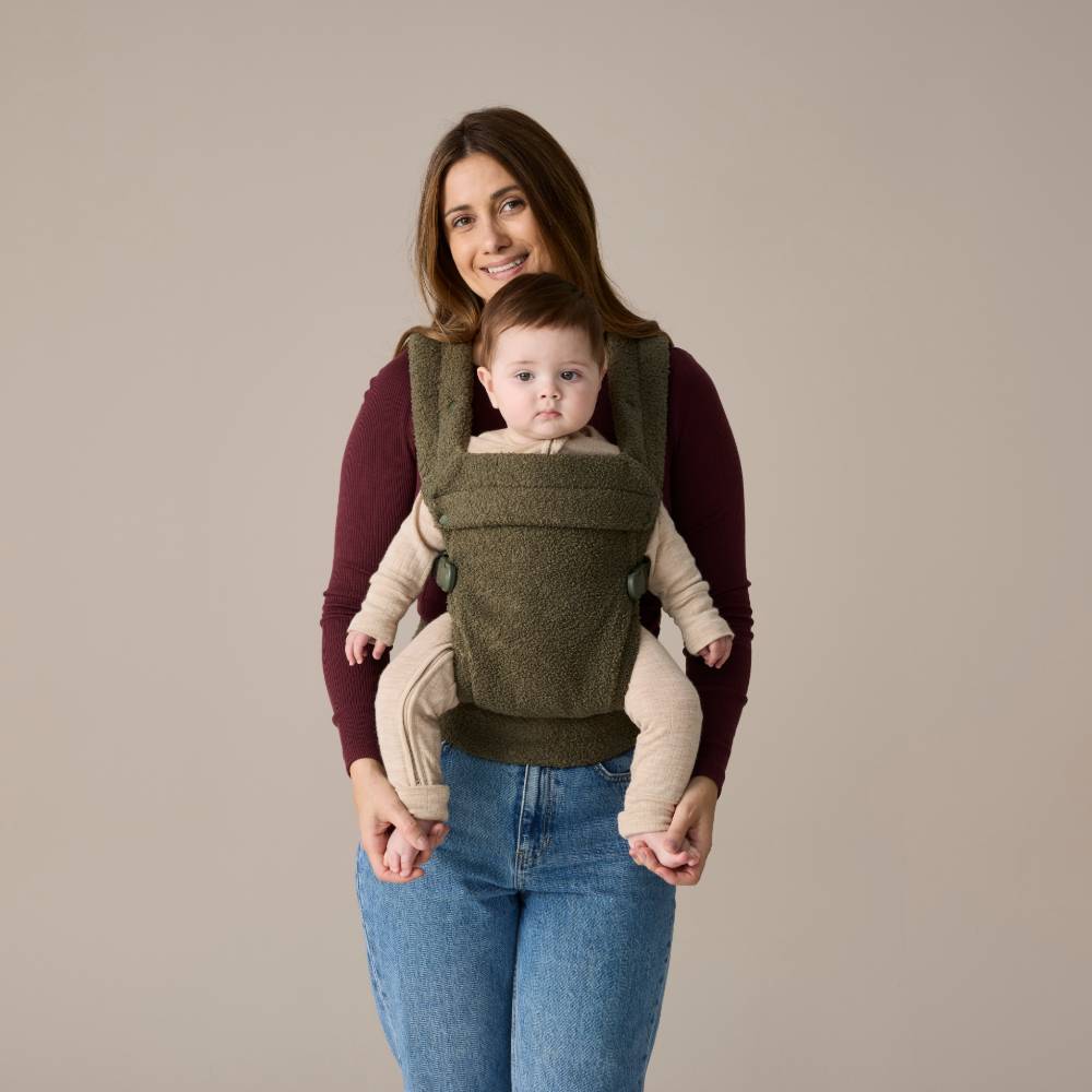 Woman carrying a baby in an olive green baby carrier against a beige background