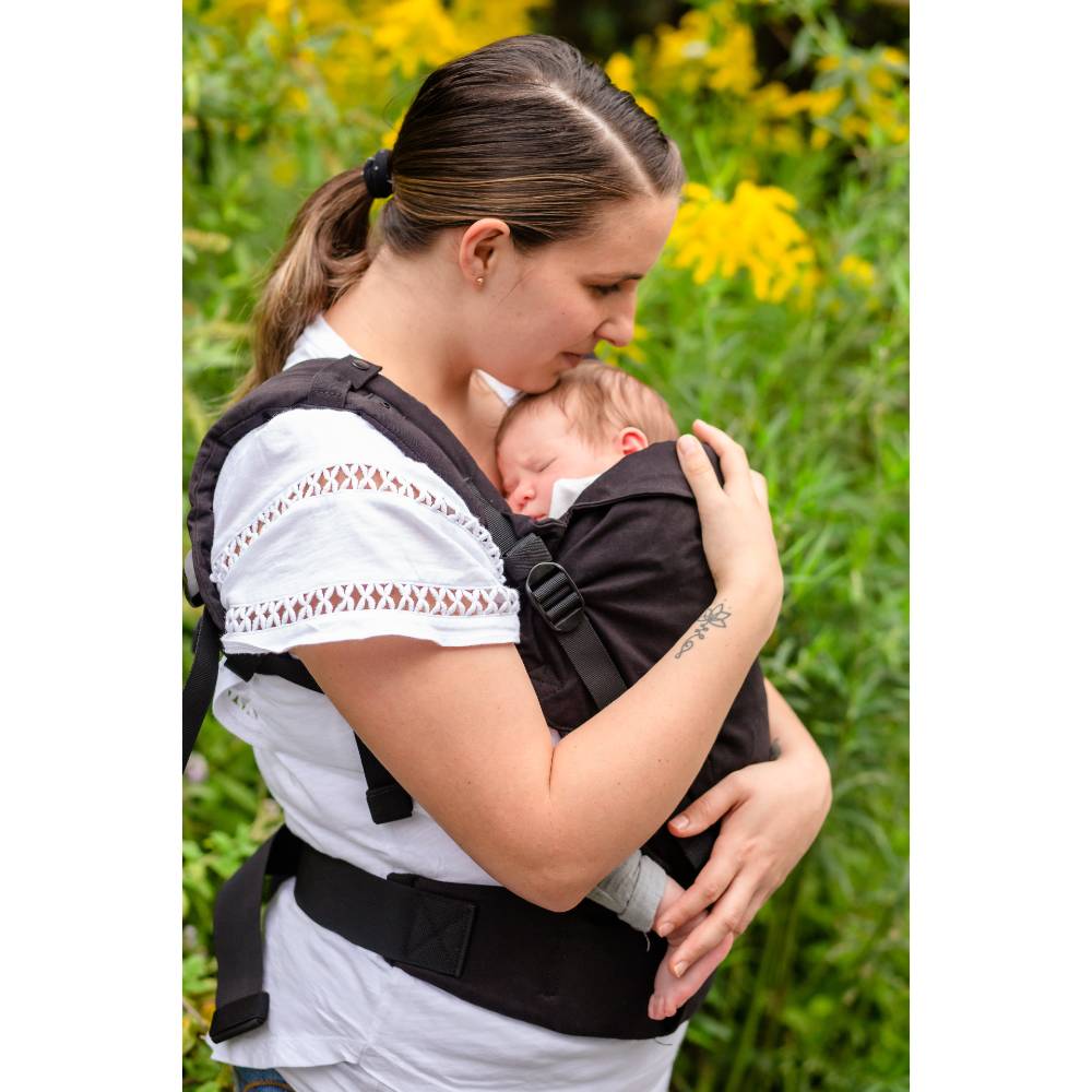 Woman carrying a baby in a black Boba X ergonomic carrier with a natural background