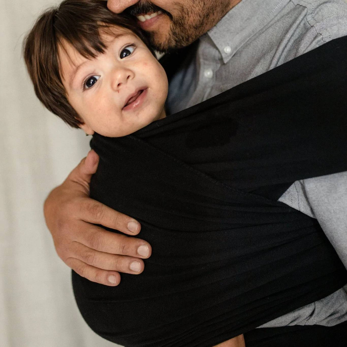 Person holding a child wearing a black outfit against a neutral background