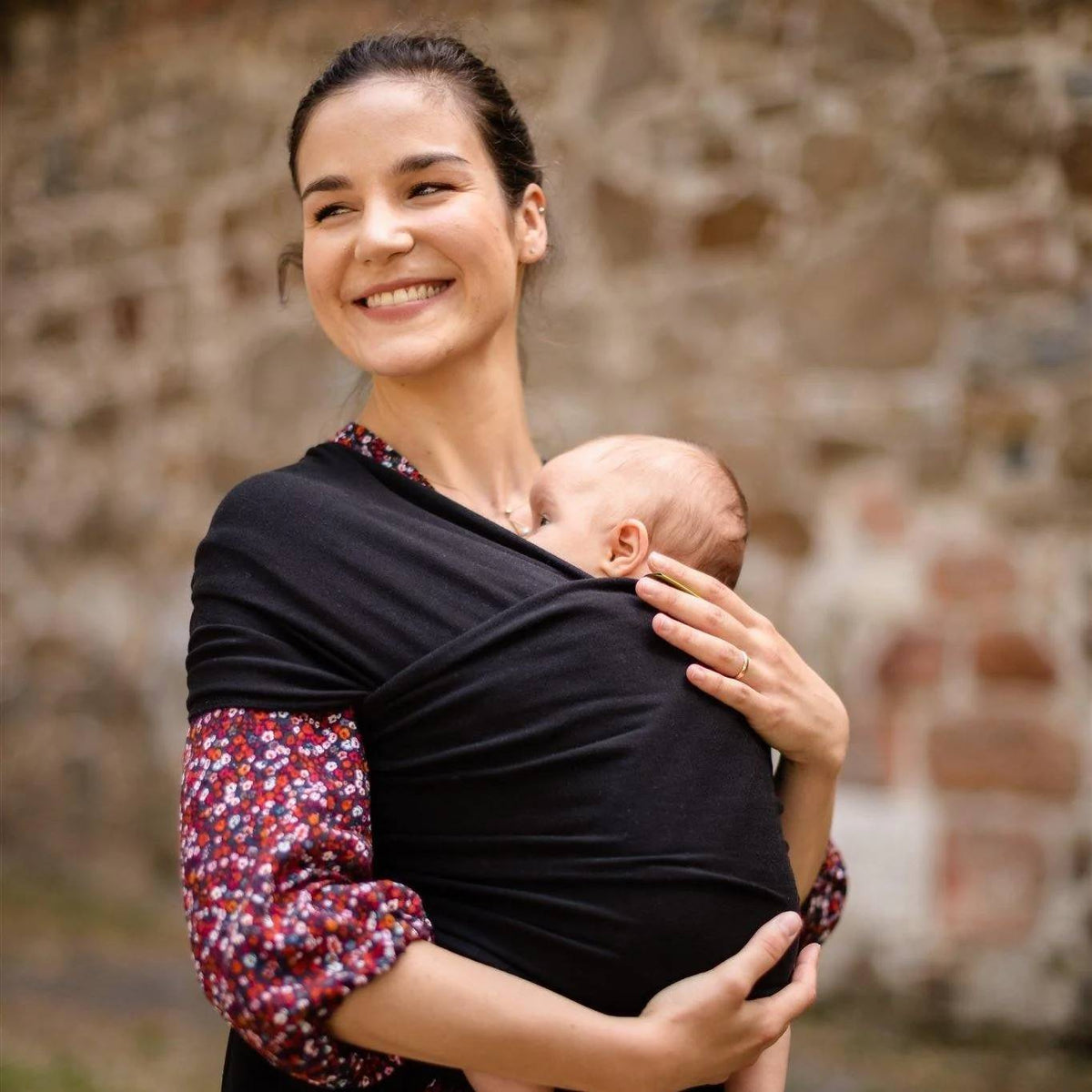 Woman holding a baby in a sling against a stone wall background