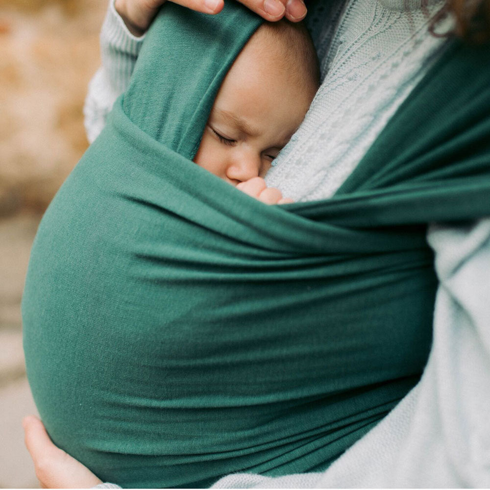 Newborn baby wrapped in a green bamboo viscose organic baby wrap sling held by a person outdoors