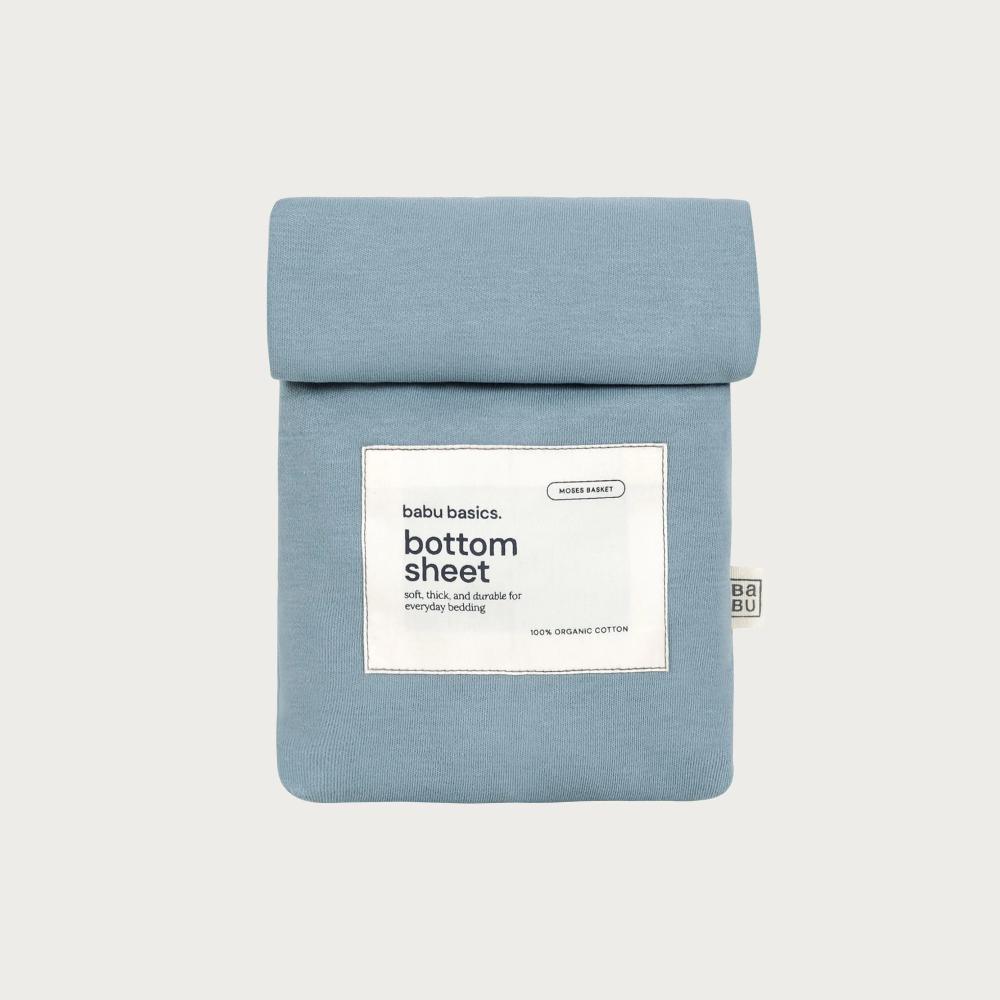 A folded light blue bottom sheet by babu basics, shown against a light gray background with a white product label on the front.