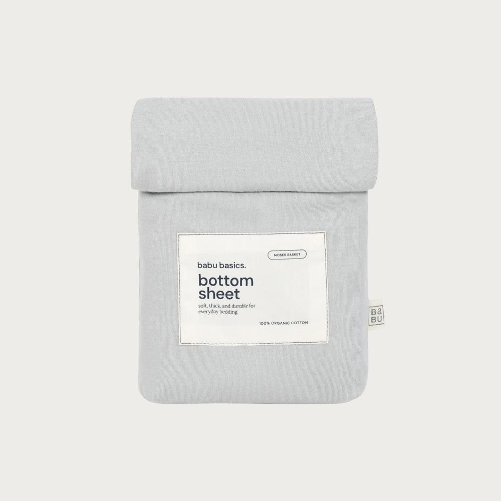 A light gray folded bottom sheet with a white paper label reading 'babu basics. bottom sheet' on a plain light gray background.