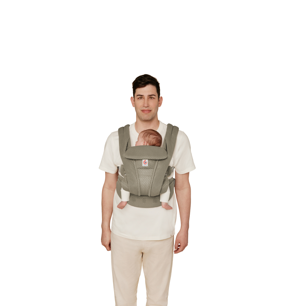 Person wearing a baby in a green baby carrier against a white background
