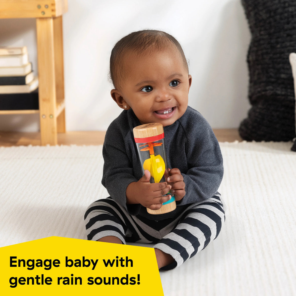 A baby holding a colourful rattle with the words 'Engage baby with gentle rain sounds!'
