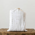 A packaged fitted cot sheet that is white with a grey pacific island inspired pattern. 