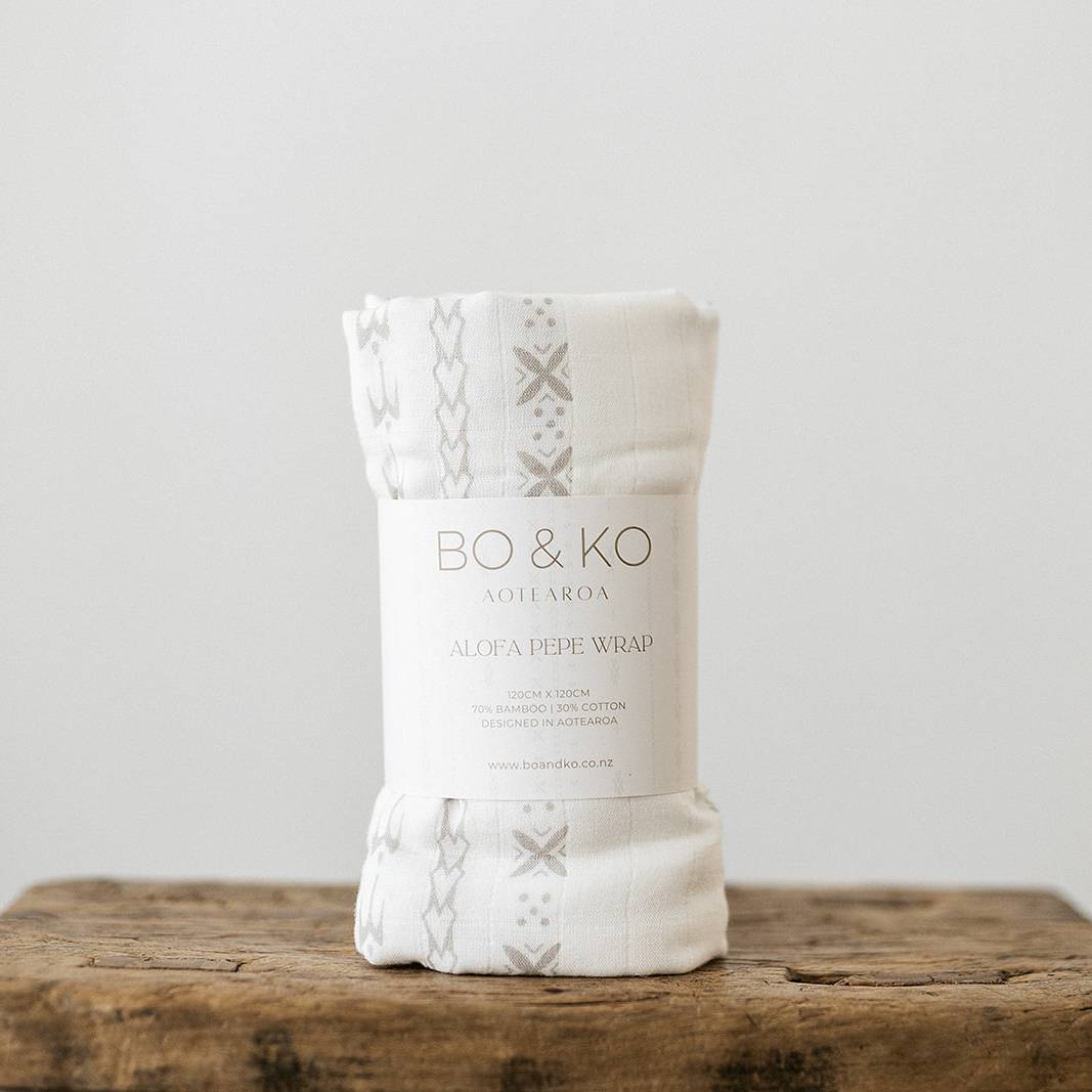 A white muslin baby swaddle wrap with pacific island inspired pattern on it. 