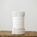 A white muslin baby swaddle with a grey maori inspired pattern on it. 