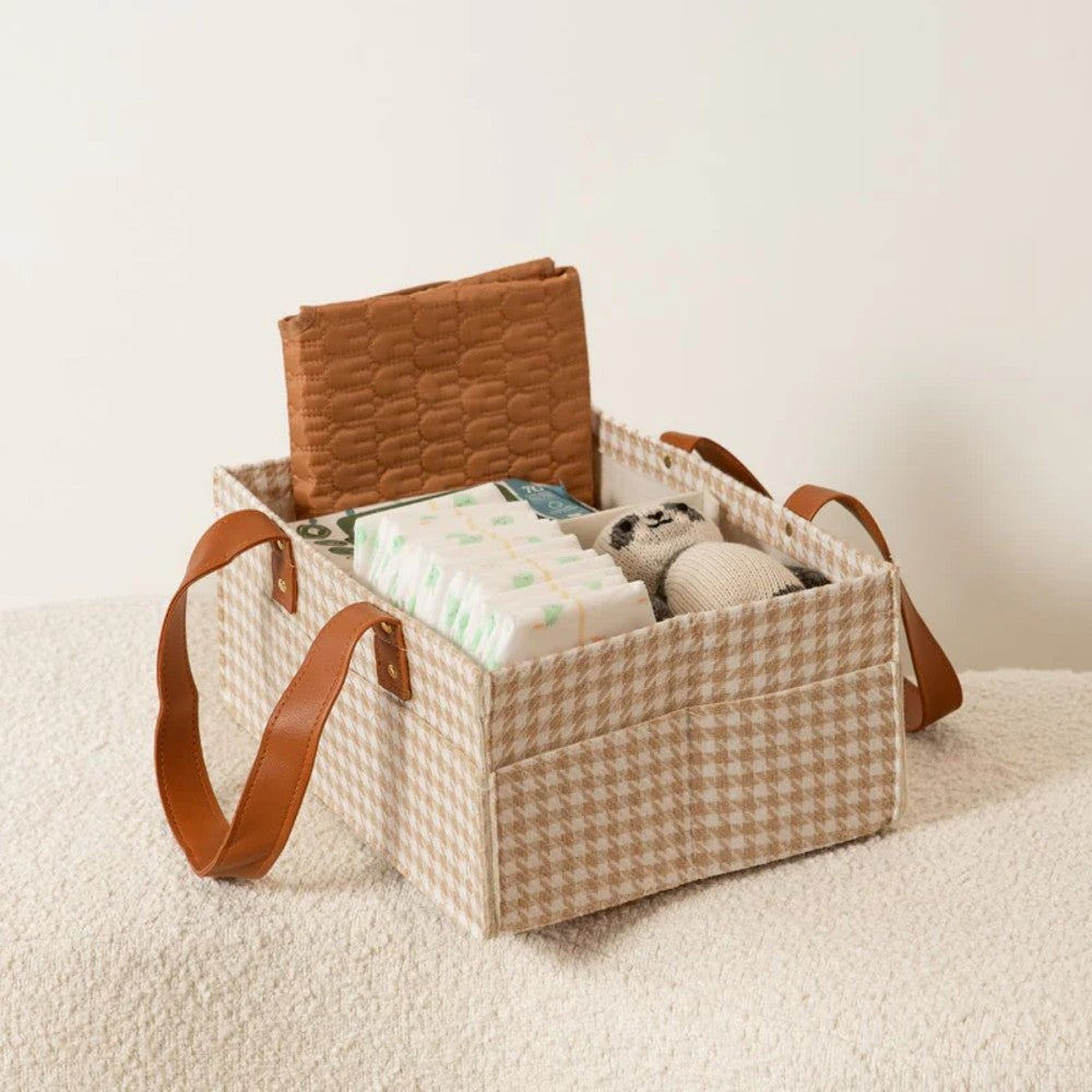Baby essentials in a checkered storage basket with brown straps on a light background