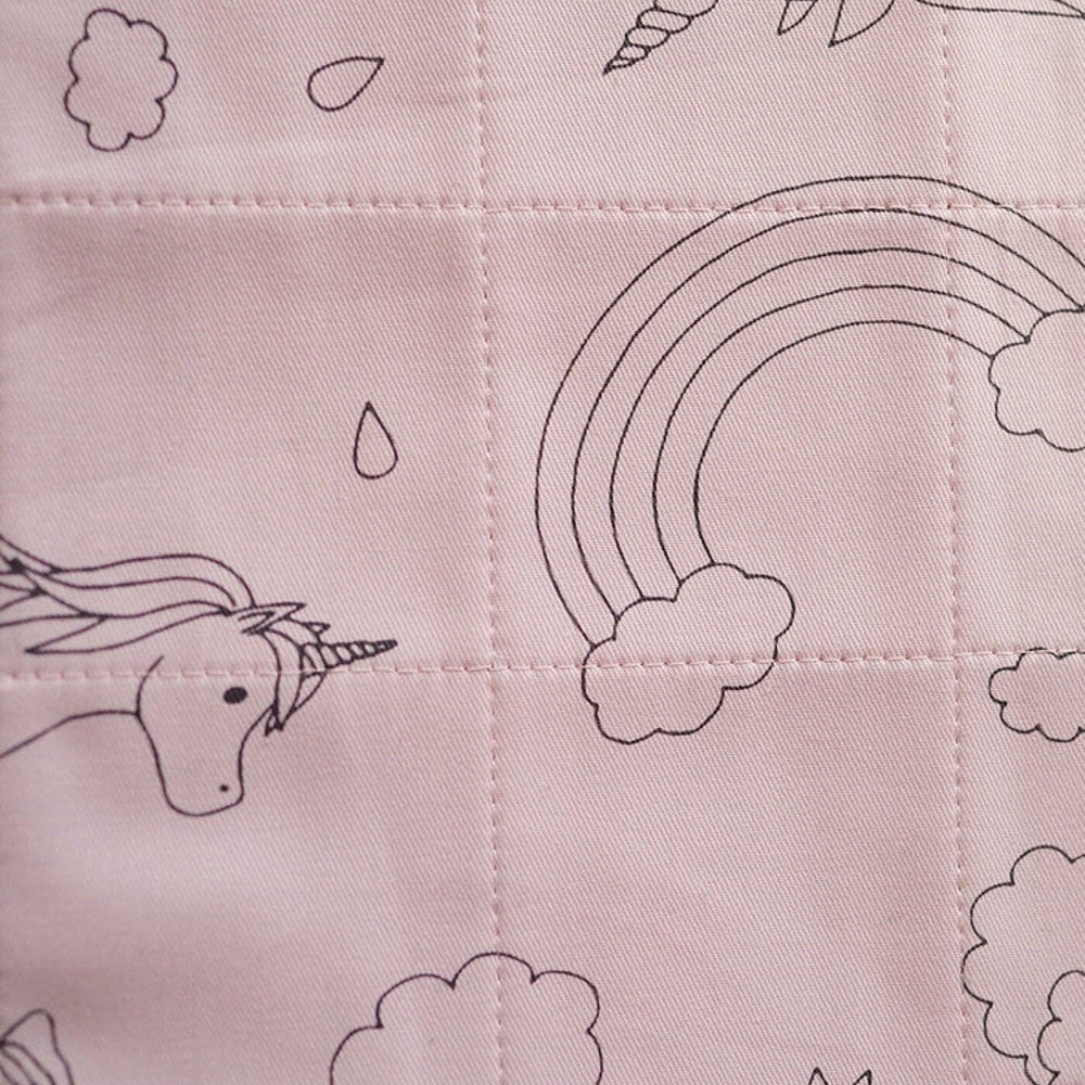 A close-up of a light pink quilted fabric featuring black line-art illustrations of unicorns, rainbows, clouds, and teardrop shapes.