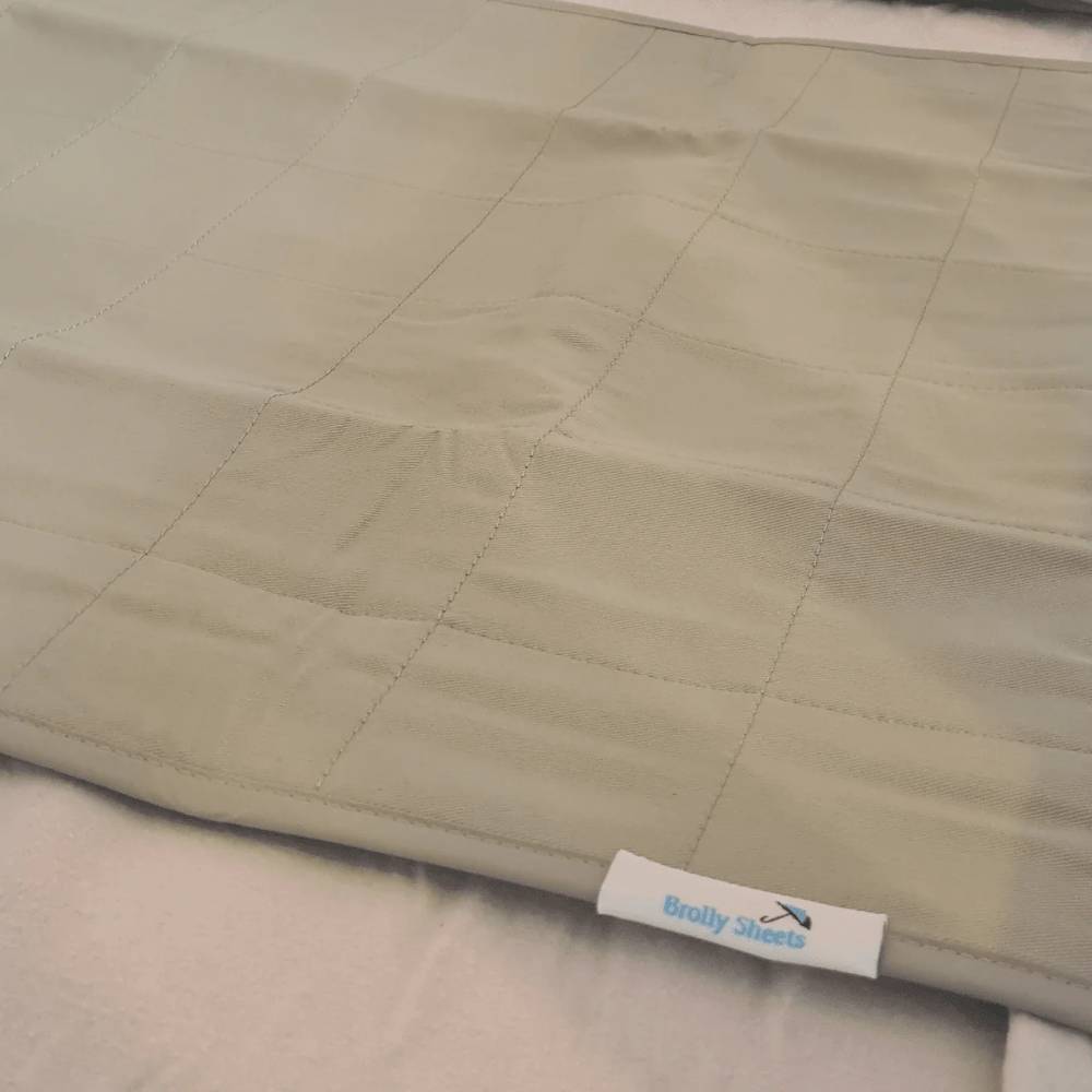 A close-up of a quilted moss green brolly sheet with a stitched grid pattern  with a white brand tag reading 'Brolly Sheets' visible near the bottom edge.