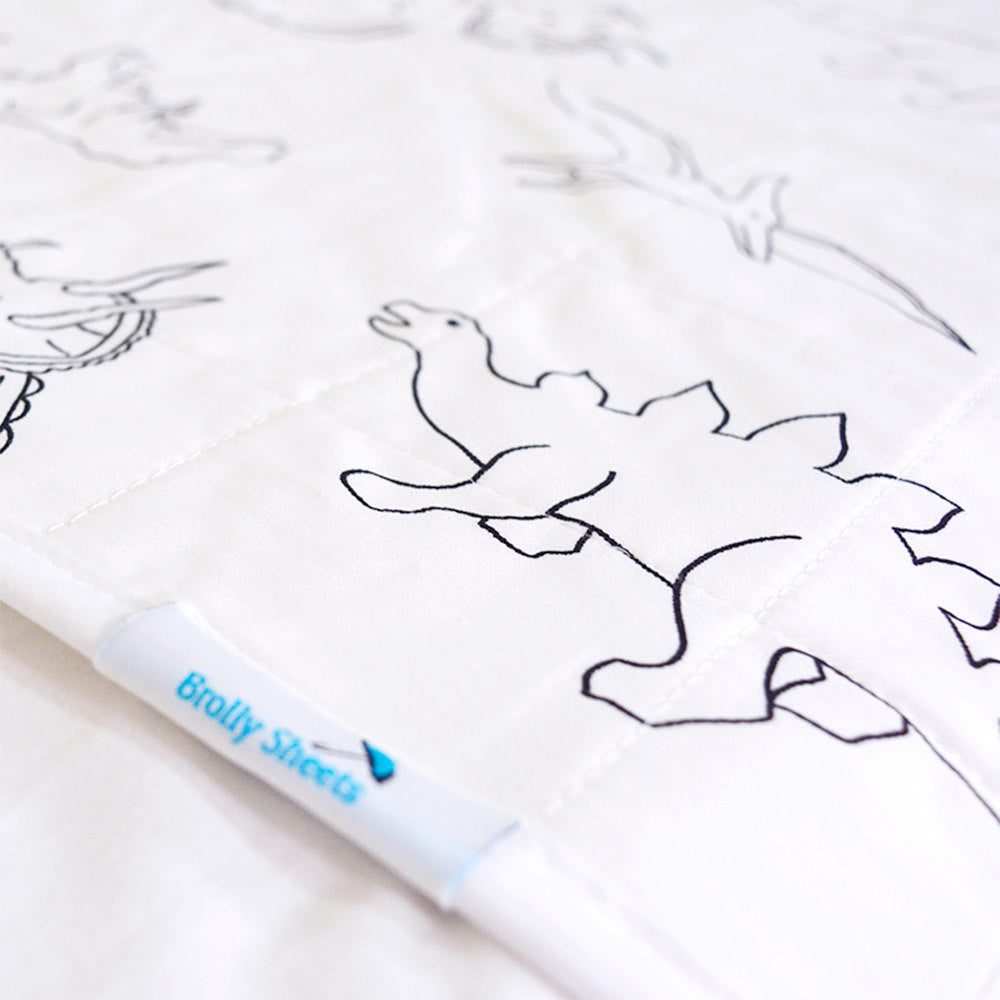 Close-up of a white quilted brolly sheet featuring black line drawings of dinosaurs, with a white fabric tag showing the brand 'Brolly Sheets'.