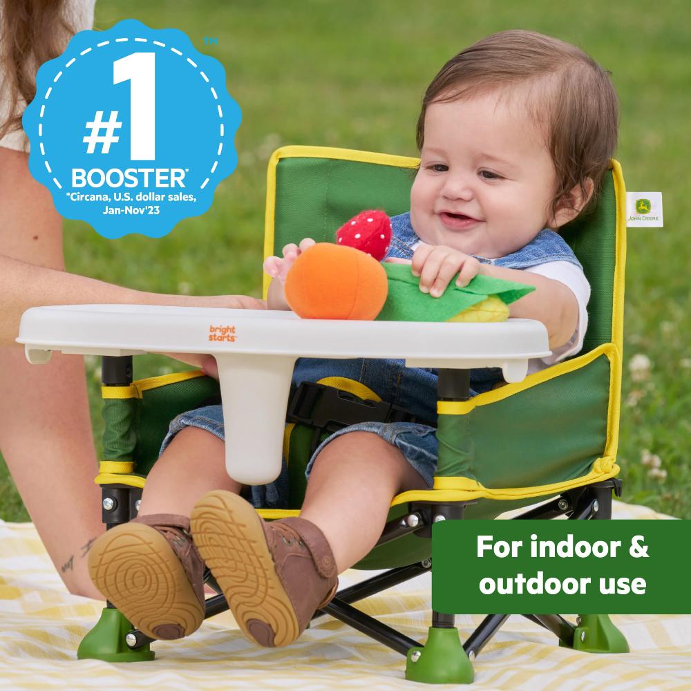 Child sitting in a green and yellow booster seat with a toy, outdoors.