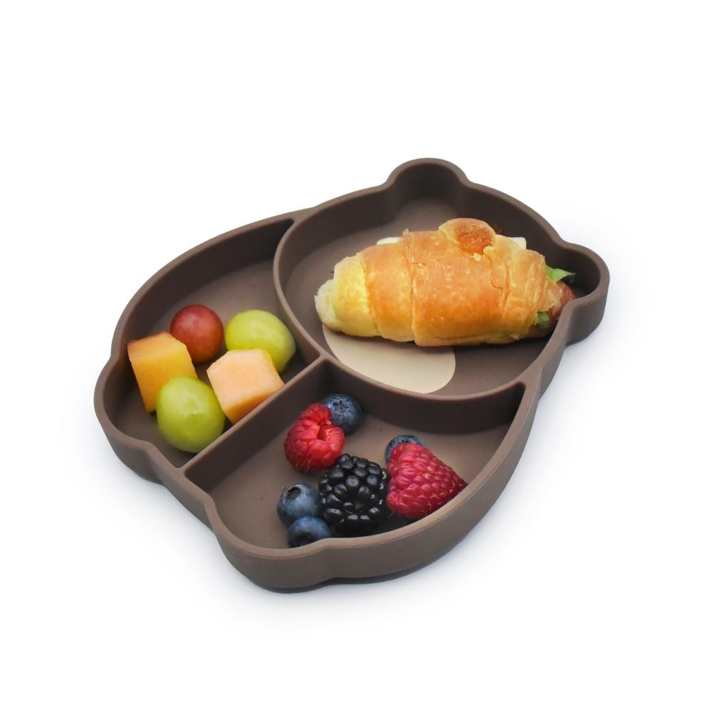 Brown divided plate with a croissant and fruits on a white background