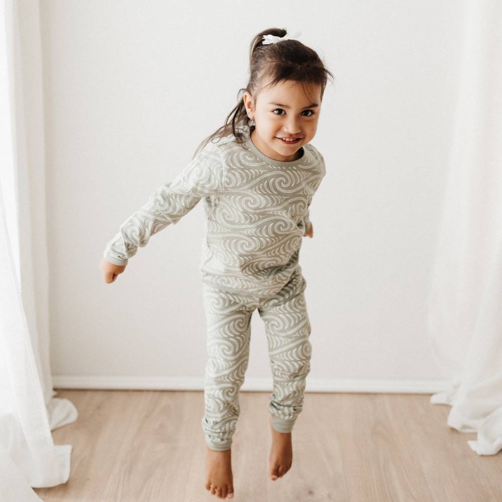 Child wearing a patterned pajama set in a room with white curtains.