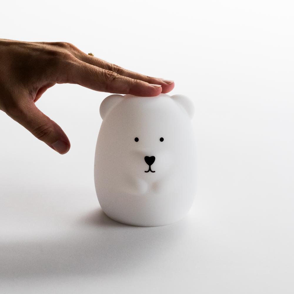 White bear-shaped night light with a hand touching it on a white background