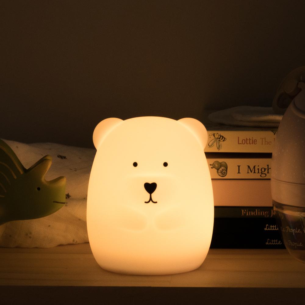 Cute bear-shaped night light on a shelf with books and a toy in the background