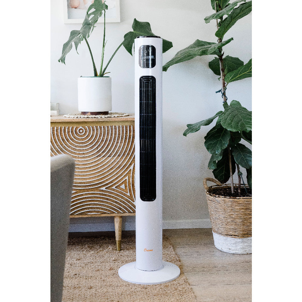 White tower fan in a room with plants and a wooden cabinet.