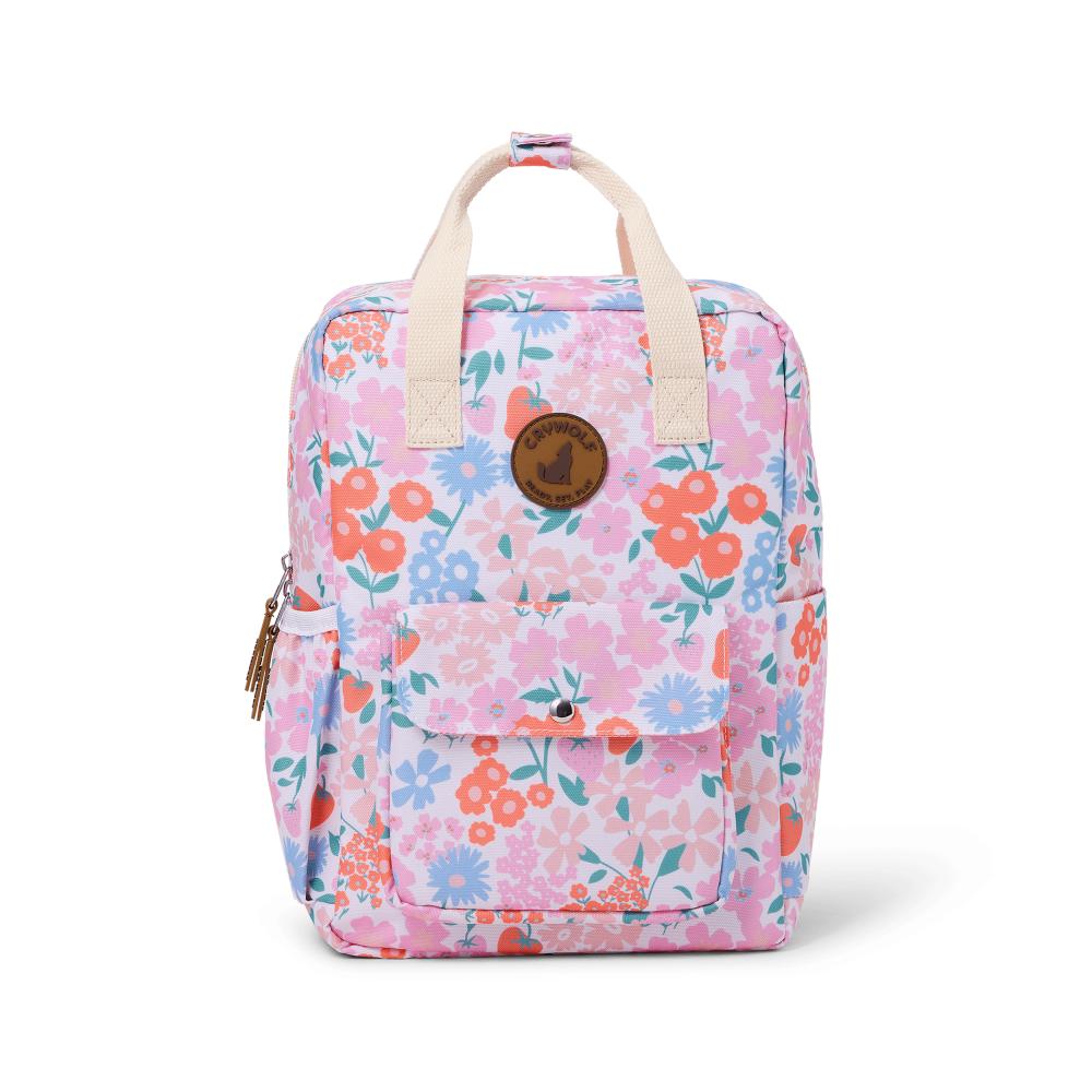 A backpack in a pink floral print with orange, blue, and green flowers, cream handles, and a brown circular logo patch on the front.
