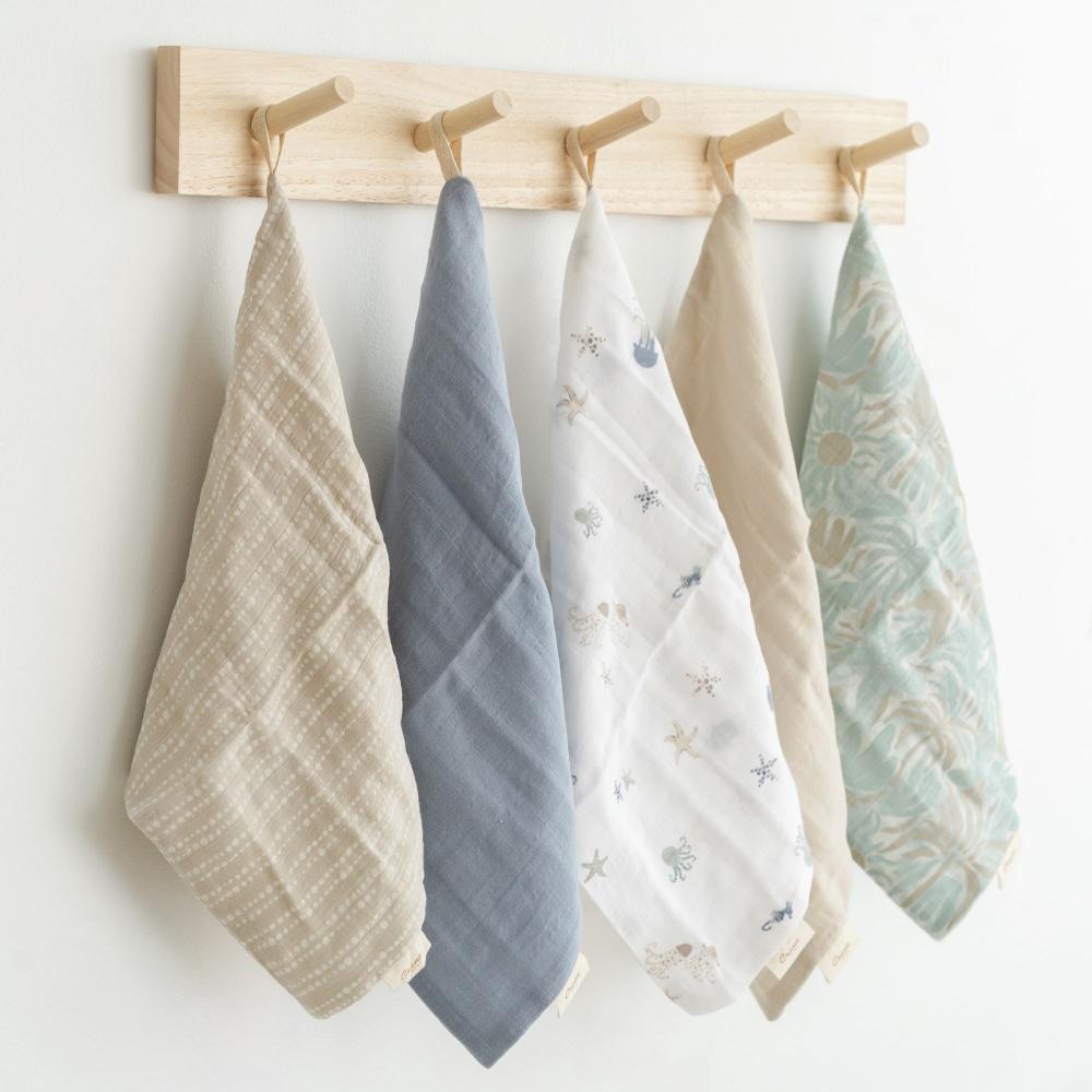 5 different coloured muslin face cloths hanging on a rack 