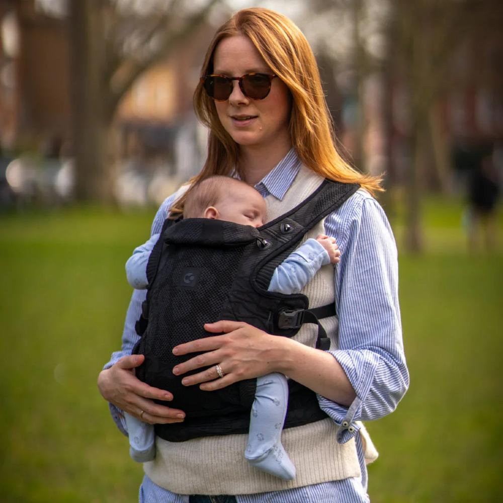 Woman holding a newborn baby in a black supportive carrier outdoors