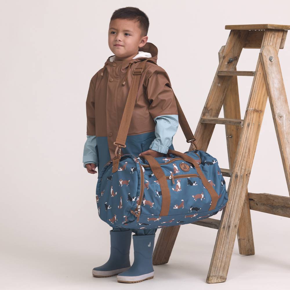Child holding a blue duffel bag with brown straps against a white background