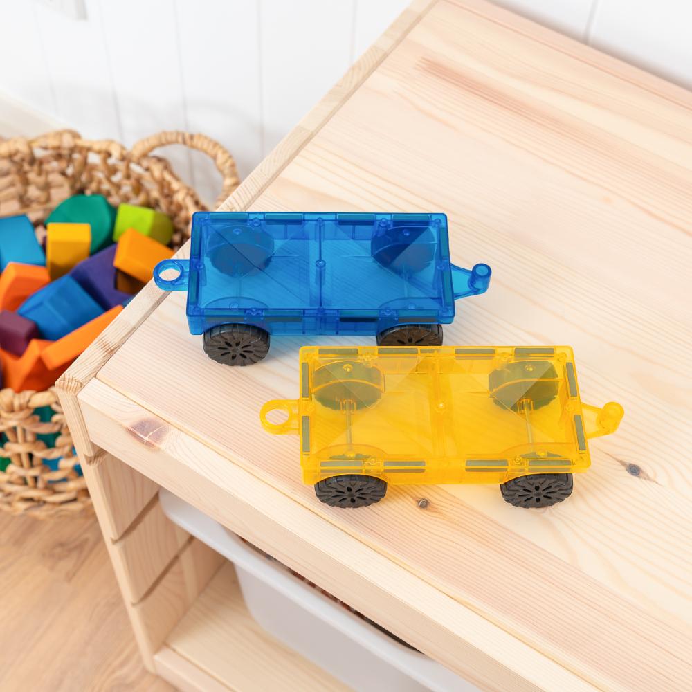Two Connetix toy trucks, one blue and one yellow, on a wooden surface with colorful blocks in the background.