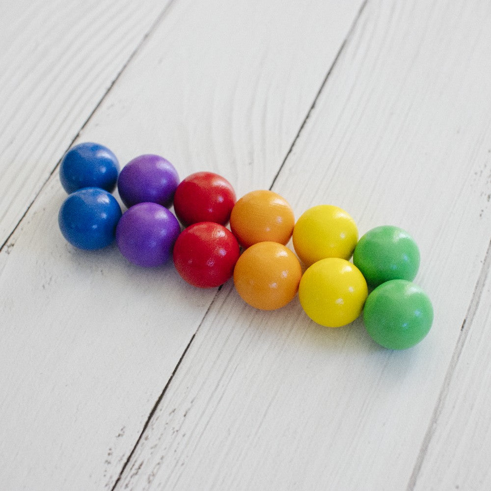 Connetix Rainbow-colored ballswith spherical beads in blue, purple, red, orange, yellow, and green, arranged on a white wooden plank surface.