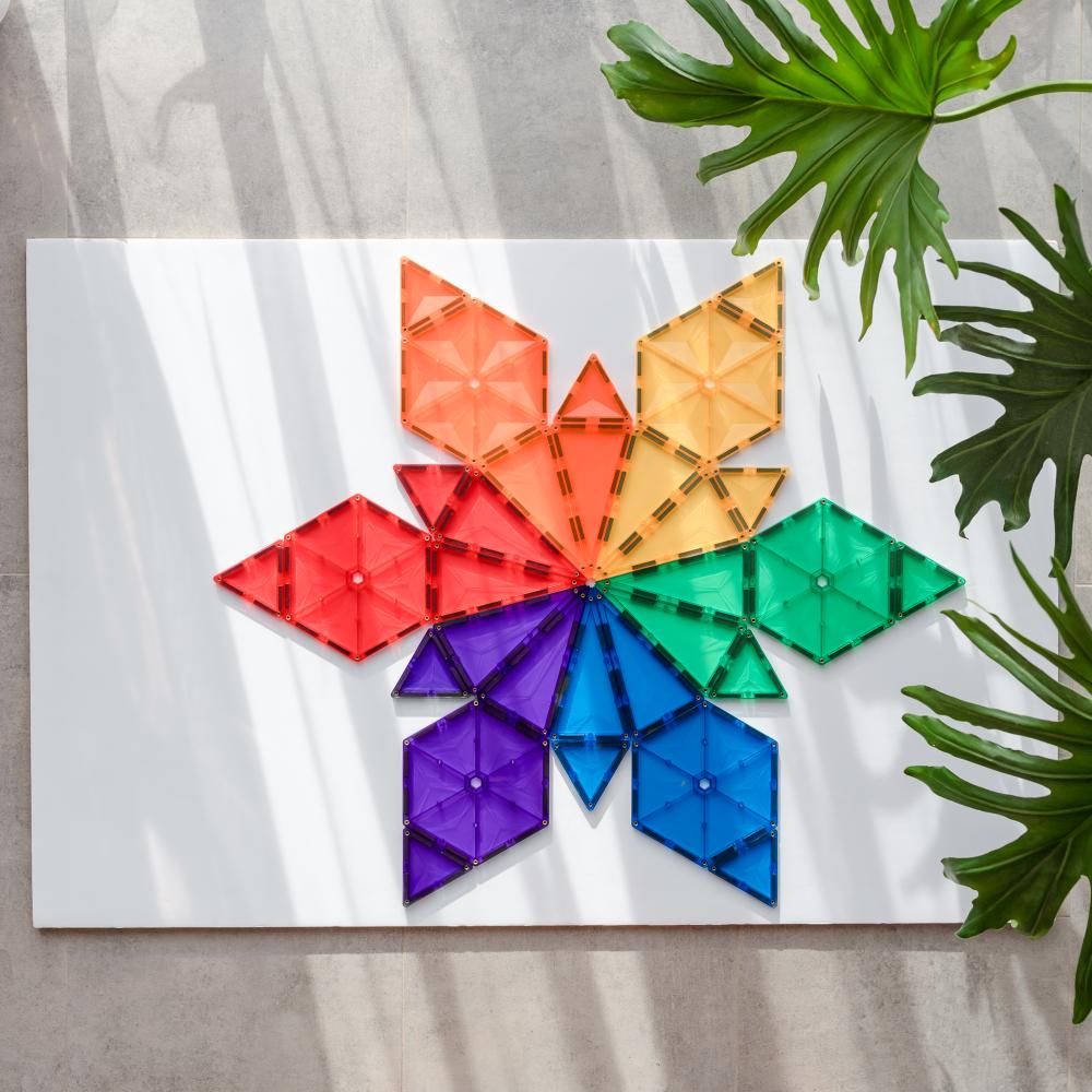 Colorful geometric shapes arranged in a circular pattern on a white surface with green leaves in the background.
