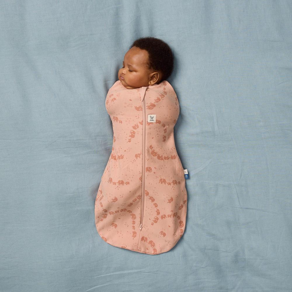 Baby sleeping in a pink patterned swaddle on a blue blanket