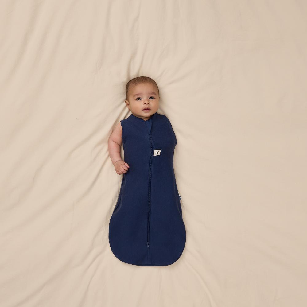 Baby lying in a navy blue sleep bag on a beige blanket