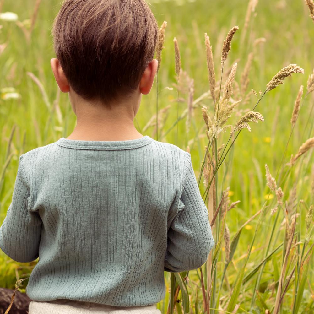 Child in a green sweater standing in a field of tall grass and wildflowers
