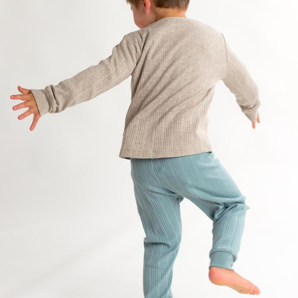 Child wearing a beige long-sleeve shirt and light blue pants on a white background