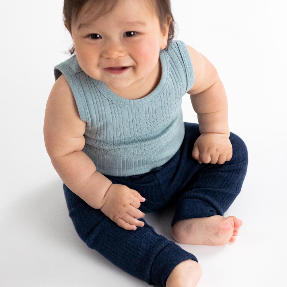 Baby wearing a light blue woolbabe singletsuit and dark blue pants on a white background
