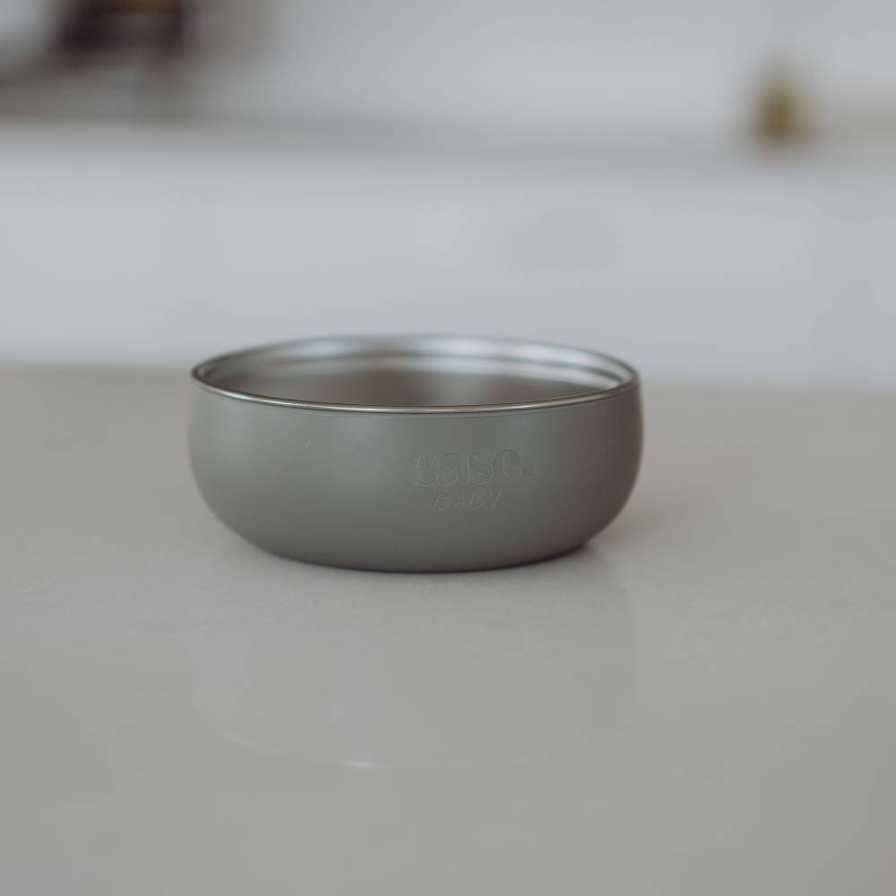 A matte gray metal small bowl with a brushed finish and embossed 'ease.baby' branding, sitting on a light beige surface with a softly blurred background.