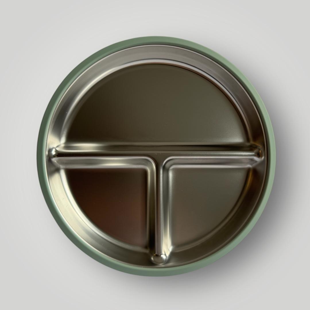 A top-down view of a round stainless steel divided plate with three compartments and a muted sage green rim, set against a neutral light gray background.
