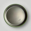 Top-down view of a round stainless steel plate with a green rim, showing the embossed 'ease.baby' logo on a light gray background.