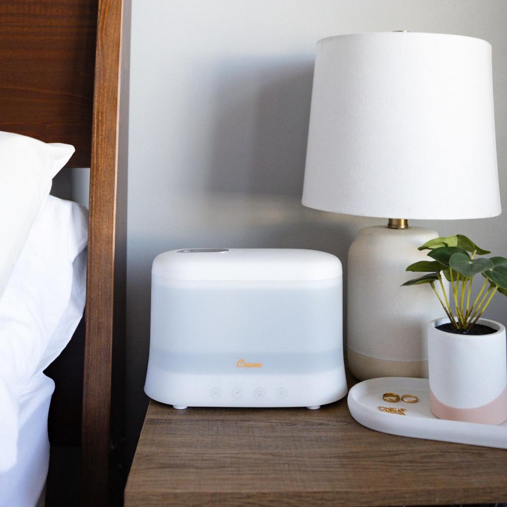 White humidifier on a nightstand next to a lamp and plant
