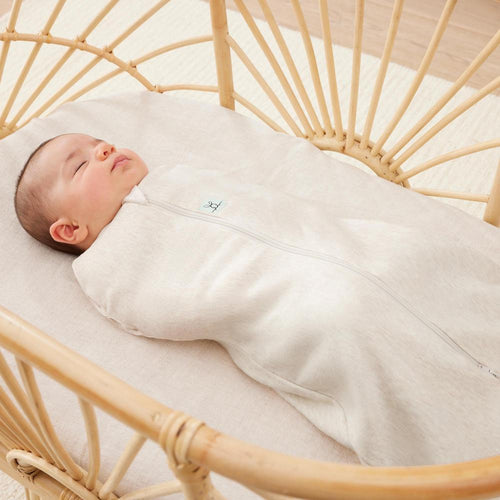 Baby swaddled in a beige swaddle with zip lying in a wooden crib