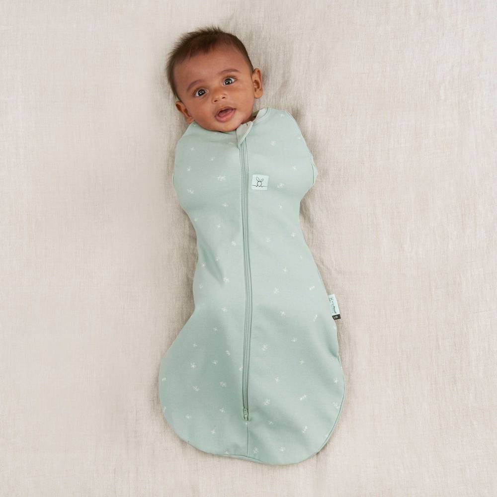Baby wrapped in a light green prem swaddle with star pattern on a beige blanket