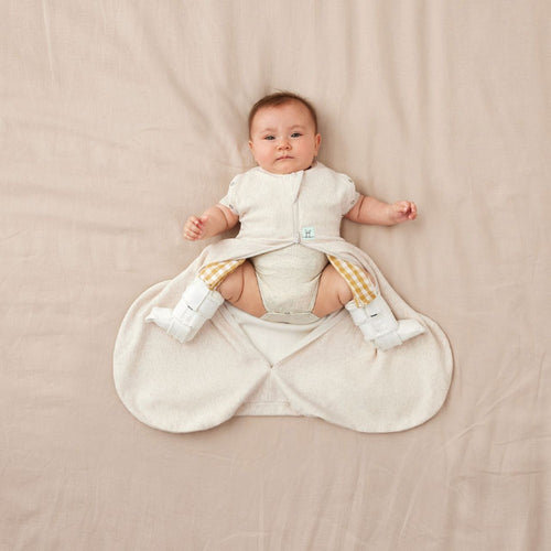 Baby in a beige baby sleeping bag for hip dysplasia with hip[ brace on a beige blanket