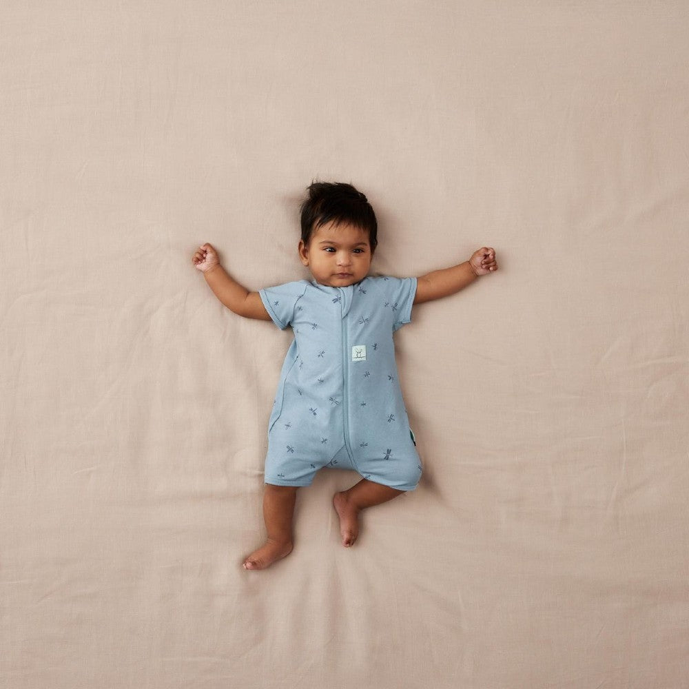 Baby wearing a light blue onesie with short sleeves on a beige blanket