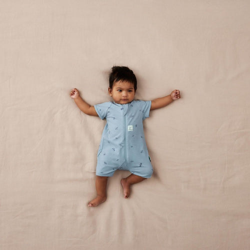 Baby wearing a light blue onesie with short sleeves on a beige blanket