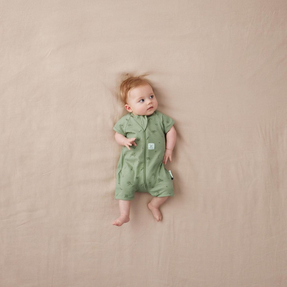 Baby wearing a green onesie lying on a beige surface
